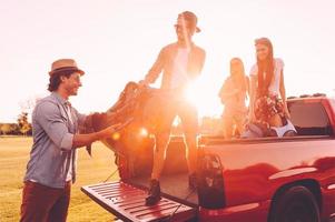 Vorbereitung vor der Reise. Schöne junge Leute, die ihre Rucksäcke auf einen Pick-up-Truck laden und mit dem Sonnenuntergang im Hintergrund glücklich aussehen foto