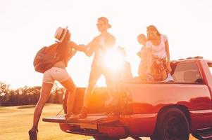 Vorbereitung auf einen großartigen Roadtrip. Schöne junge Leute bereiten sich auf einen Roadtrip vor, während ein fröhlicher Mann der Frau hilft, zum Pick-up-Truck zu gelangen foto