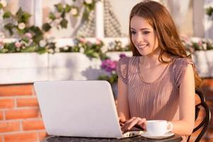 kostenloses WLAN nutzen. schöne junge frau, die im café im freien sitzt und laptop verwendet foto