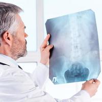 Röntgen untersuchen. Rückansicht eines selbstbewussten Arztes mit reifen grauen Haaren, der das Röntgenbild untersucht, während er isoliert auf Weiß steht foto