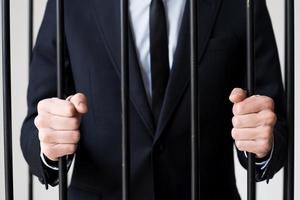 Geschäftsleute im Gefängnis. Zugeschnittenes Bild eines Mannes in Abendgarderobe, der hinter einer Gefängniszelle steht foto