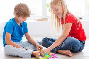 kinder spielen zu hause. Zwei süße kleine Kinder spielen mit bunten Plastikbuchstaben, während sie auf dem Hartholzboden sitzen foto