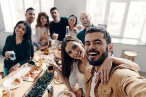 glückliche Momente teilen. Selbstporträt von jungen Menschen in Freizeitkleidung, die lächeln, während sie drinnen eine Dinnerparty haben foto