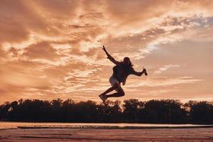 wilder junger mann, der gegen den dramatischen himmel schwebt, während er auf den pier springt foto