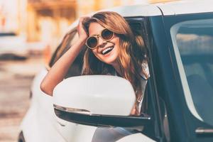 nur Straße voraus. Schöne junge, fröhliche Frauen, die mit einem Lächeln in die Kamera schauen, während sie in ihrem Auto sitzen foto