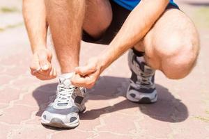 Schnürsenkel binden. Nahaufnahme eines Mannes, der Schnürsenkel an Sportschuhen bindet, während er im Freien steht foto