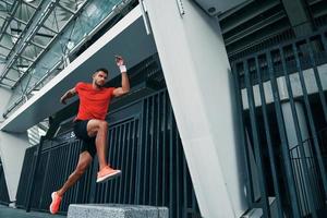 volle Länge der sportlichen jungen Frau in Sportkleidung, die beim Training im Freien in einem Weitsprung schwebt foto