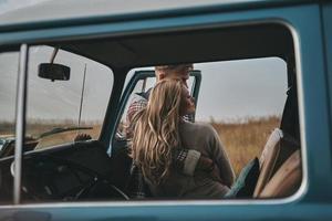 enge Beziehung... schönes junges Paar, das sich umarmt, während es draußen in der Nähe des Minivans im Retro-Stil steht foto