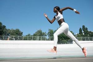 Selbstbewusste junge Afrikanerin in Sportkleidung, die im Freien auf der Strecke läuft