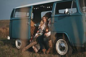 genießen ihre gemeinsame Zeit. hübscher junger Mann, der Gitarre hält und seine schöne Freundin umarmt, während er in einem blauen Minivan im Retro-Stil sitzt foto