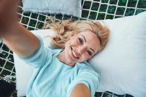 Draufsicht der schönen jungen lächelnden Frau, die selfie beim Entspannen in der großen Hängematte macht foto