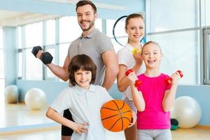 glücklich und sportlich. glückliche familie, die verschiedene sportgeräte hält, während sie im fitnessclub nahe beieinander stehen foto