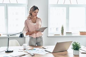 jeden Tag neue Entscheidungen. Schöne junge Frau in eleganter Freizeitkleidung, die mit einem digitalen Tablet arbeitet, während sie in einem modernen Büro steht foto