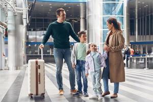 ganze Familie mit zwei kleinen Kindern, die am Flughafenterminal auf ihren Flug warten foto