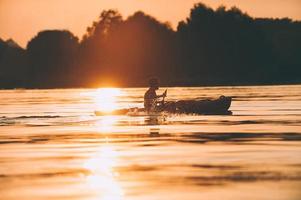 Treffen Sie den besten Sonnenuntergang. Seitenansicht des Mannes, der auf dem Fluss Kajak fährt, mit Sonnenuntergang im Hintergrund foto