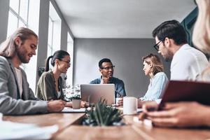 begeistert von ihrem Projekt. Gruppe junger moderner Menschen in eleganter Freizeitkleidung, die während der Arbeit im Kreativbüro über Geschäfte diskutieren foto