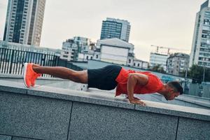 Selbstbewusster junger Mann in Sportkleidung, der beim Training im Freien die Plankenposition hält foto