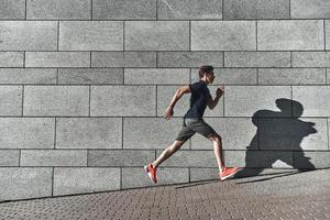 Morgentraining. Volle Länge des jungen Mannes in Sportkleidung, der beim Training draußen läuft foto