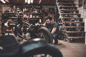 Mann repariert Fahrrad. Selbstbewusster junger Mann, der Motorrad in der Werkstatt repariert foto