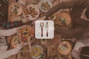 perfektes Abendessen. Digital komponiertes Bild von Küchenutensilien über Draufsicht von vier Personen, die zusammen zu Abend essen, während sie am rustikalen Holztisch sitzen foto