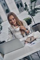 Leidenschaft für ihr Projekt. Draufsicht einer jungen Frau, die einen Laptop benutzt und Kaffee trinkt, während sie im modernen Restaurant sitzt foto