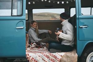 Reiselied singen. hübscher junger mann, der gitarre für seine schöne freundin spielt, während er in einem blauen minivan im retro-stil sitzt foto
