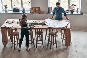 Geschäftsideen teilen. Draufsicht auf junge Kollegen in eleganter Freizeitkleidung mit Blaupause während der Arbeit im kreativen Arbeitsbereich foto