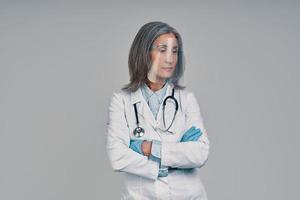 Reife schöne Ärztin im Gesichtsschutz, die die Arme verschränkt hält foto