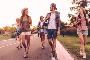 auf der Suche nach Abenteuern. Gruppe junger Leute mit Rucksäcken, die zusammen auf der Straße spazieren und glücklich aussehen foto