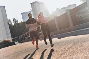 bestes Joggen aller Zeiten. volle Länge des jungen Paares in der Sportkleidung, die zusammen durch die Stadtstraße läuft foto