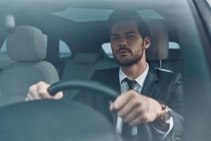 ich freue mich auf. hübscher junger mann im vollen anzug, der beim autofahren geradeaus schaut foto