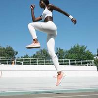 Selbstbewusste junge Afrikanerin in Sportkleidung, die im Freien auf die Strecke springt