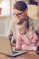 Geschäftsplan mit Mama erstellen. Kleines Mädchen mit Laptop, während sie mit ihrer Mutter im Büro auf dem Schreibtisch sitzt foto