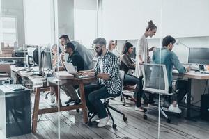 kreatives Business-Team. Gruppe junger Geschäftsleute, die zusammen arbeiten und kommunizieren, während sie an ihren Arbeitsplätzen im Büro sitzen foto