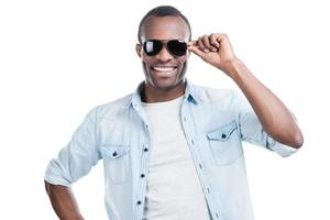 bereit, Herzen zu gewinnen. hübscher junger schwarzer Mann, der seine Sonnenbrille anpasst und in die Kamera lächelt, während er vor weißem Hintergrund steht foto