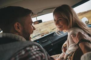 echte Liebe. Fröhliches junges Paar lacht, während es auf den Beifahrersitzen im Minivan im Retro-Stil sitzt foto