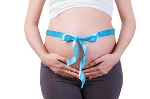 das beste geschenk überhaupt. Zugeschnittenes Bild einer schwangeren Frau mit blauem Band auf ihrem Bauch, die isoliert auf Weiß steht foto