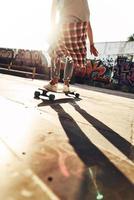 Nahaufnahme der Rückseite des modernen jungen Mannes, der beim Skateboarden im Skatepark im Freien rumhängt foto