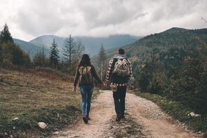 immer nebeneinander. Rückansicht in voller Länge von jungen Paaren, die beim Wandern in den Bergen Händchen halten foto