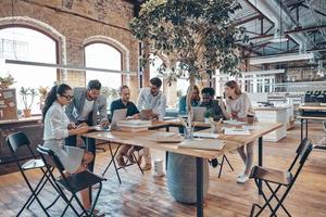 Gruppe junger moderner Menschen in eleganter Freizeitkleidung, die bei der Arbeit im Büro kommunizieren und moderne Technologien nutzen foto