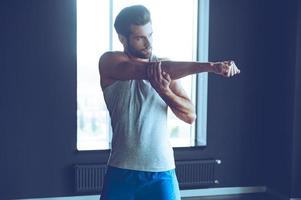 gutes Aufwärmen. Junger gutaussehender Mann in Sportbekleidung, der seinen Arm im Fitnessstudio streckt foto