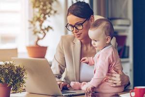 zusammen arbeiten. junge schöne Geschäftsfrau mit Laptop, während sie mit ihrem kleinen Mädchen an ihrem Arbeitsplatz sitzt foto