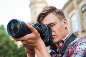 den Moment festhalten. hübscher junger Mann, der ein Foto mit seiner Digitalkamera macht, während er im Freien steht