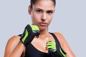 sich verteidigt. attraktive junge sportliche Frau in Sporthandschuhen posiert vor grauem Hintergrund foto