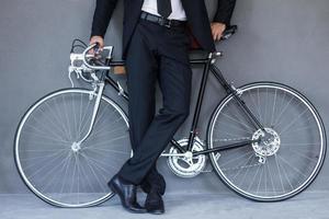 Geschäft auf Rädern. Zugeschnittenes Bild eines jungen Geschäftsmannes, der sich am Fahrrad lehnt, während er vor grauem Hintergrund steht foto