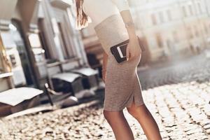 beschäftigt in der Stadt. Nahaufnahme einer jungen Frau, die ihr Smartphone und ihre Brieftasche trägt, während sie im Freien spazieren geht foto