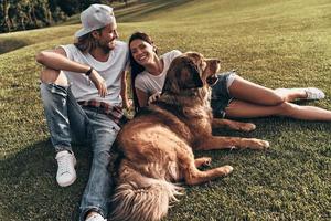 gute zeit zusammen. junges modernes paar, das mit seinem hund auf dem gras liegt, während es seine freizeit im park verbringt foto