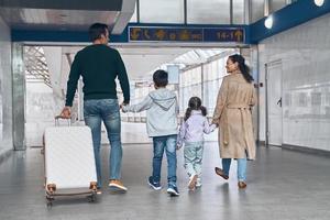 Rückansicht der Familie mit zwei kleinen Kindern in voller Länge, die am Flughafenterminal spazieren gehen foto