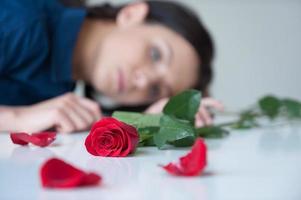 einsam fühlen. schöne junge Frau, die am Tisch sitzt und eine rote Rose darauf liegt foto