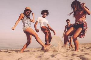 aktives Spiel am Strand. Gruppe fröhlicher junger Leute, die am Strand mit Fußball spielen foto